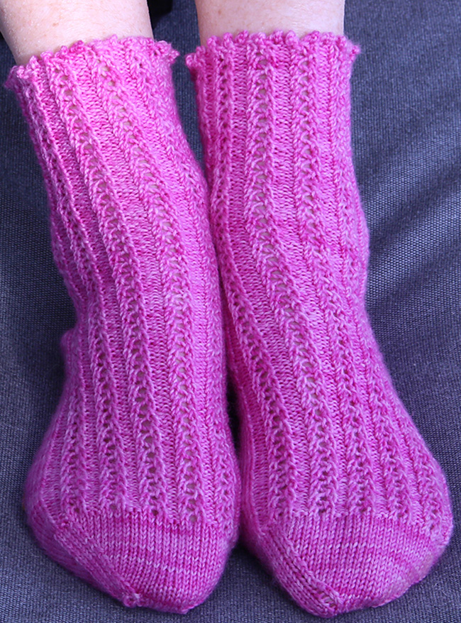 Ripple Rib Socks knitted in Raspberry cordial pink coloured yarn on two feet.
