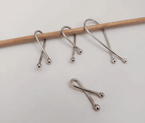 The three larger sizes of stitch markers on a needle that is slightly too big for the Extra Small size. The Extra Small stitch marker is below on a white background.