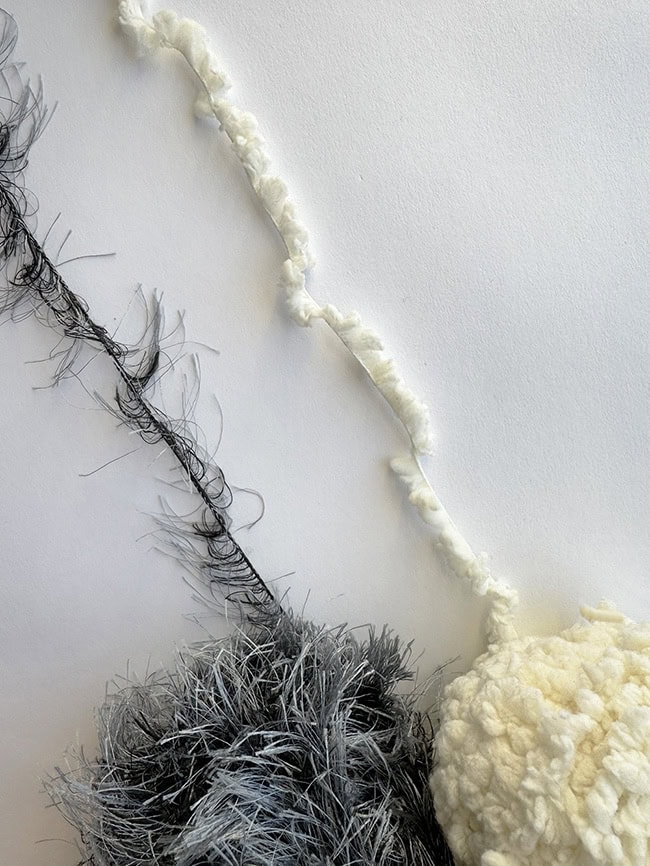 A string of black eyelash yarn next to a string of white faux fur yarn.