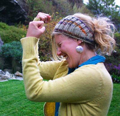 blonde white lady in a blue shirt and yellow cardigan, wearing a wide knited headband with a messy ponytail and large round earrings